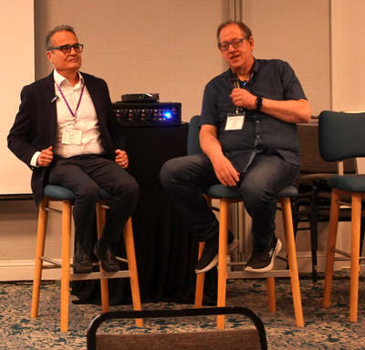 Two people seated on stools, one holding a microphone